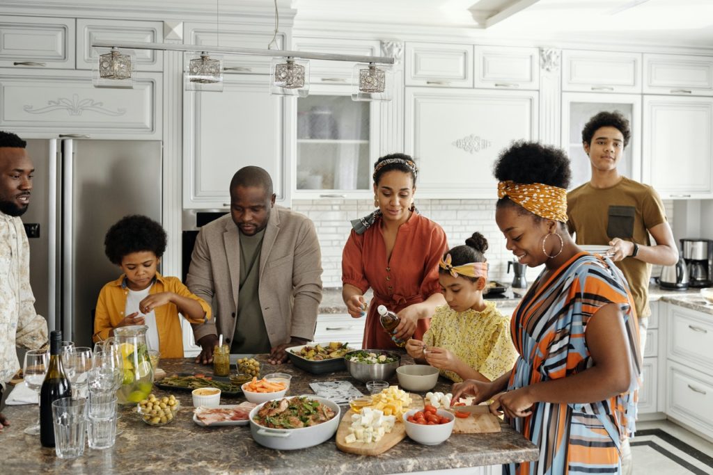 A black family, helping each other prepare food in the kitchen.