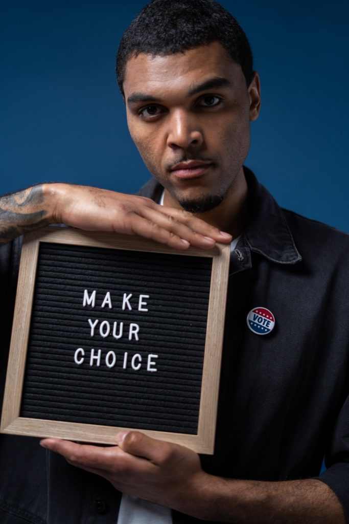 A man holding a writing in a wooden frame that says 'make your choice'